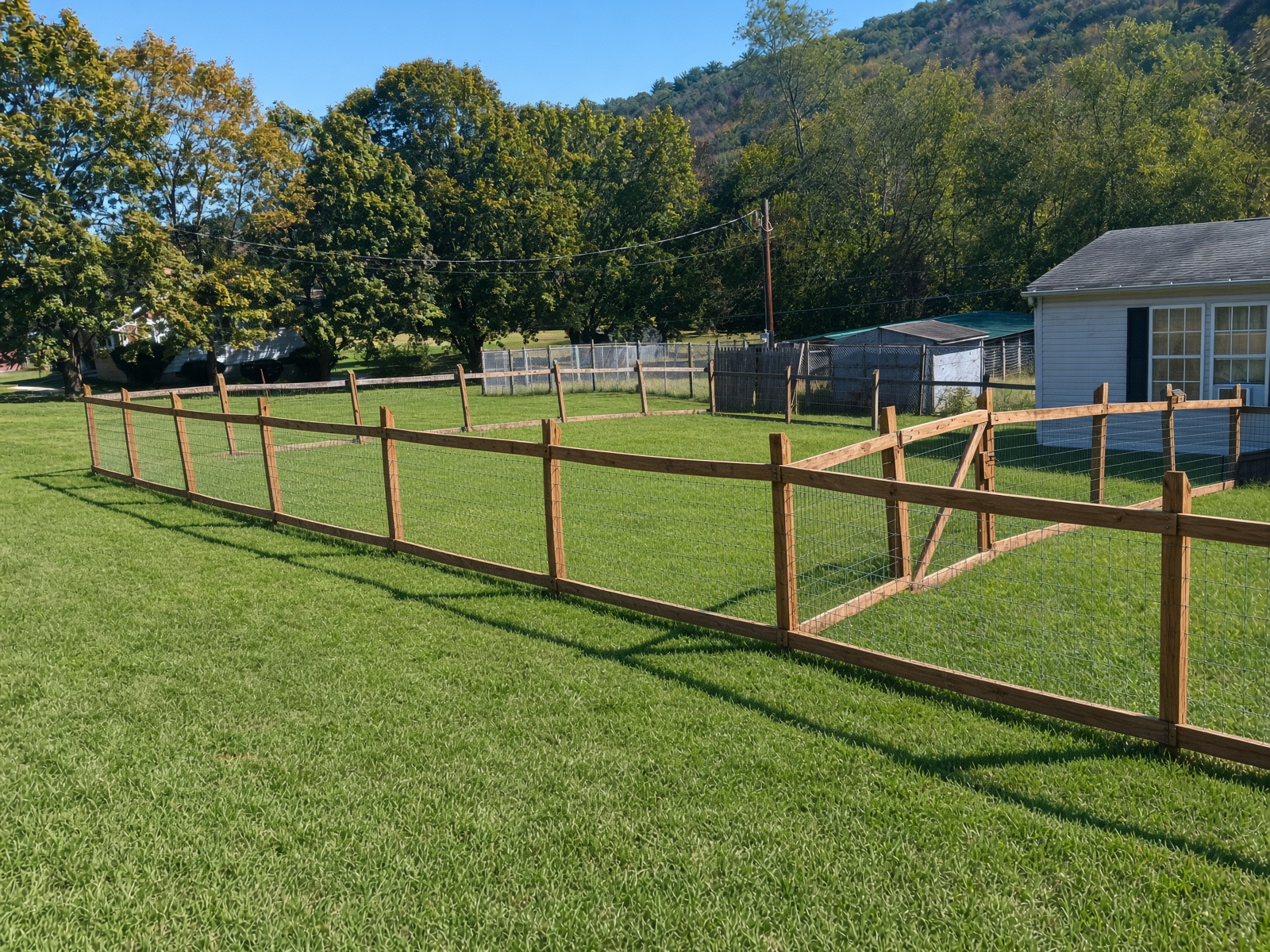 Long run of wire fencing with wooden posts across open yard